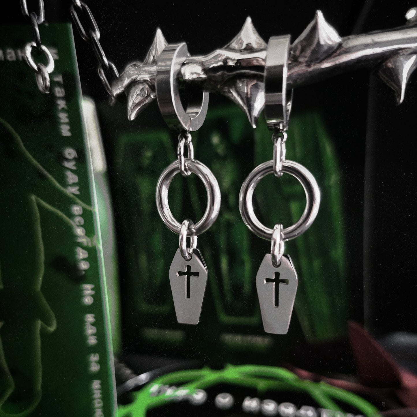 Silver earrings with coffin and cross charms on a dark background