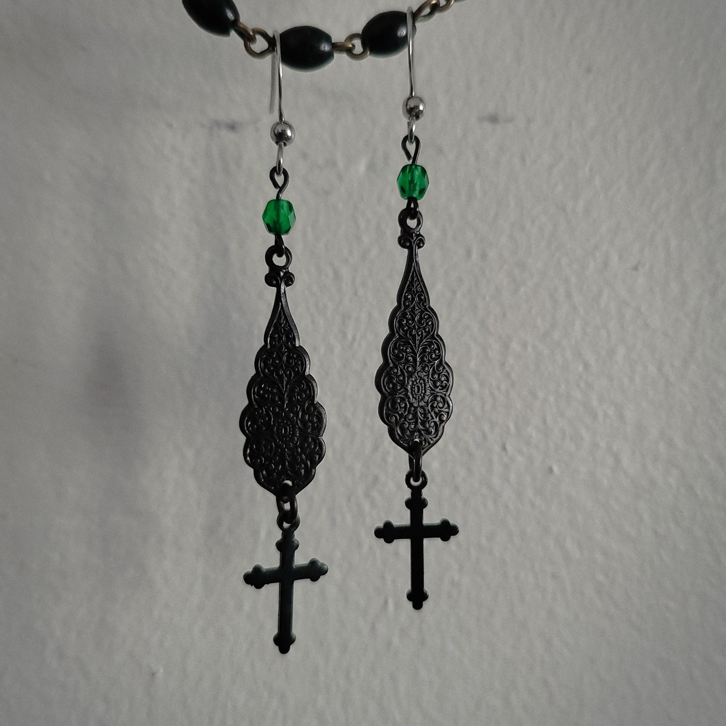 Black filigree earrings with green beads on a plain background