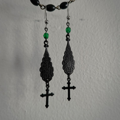 Black filigree earrings with green beads on a plain background