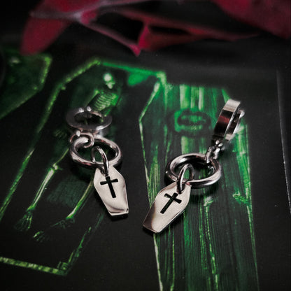 Silver coffin charms with cross designs on a dark surface