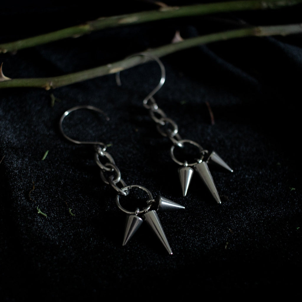 Pair of silver earrings dangling with short and long spikes hanging from chain links.