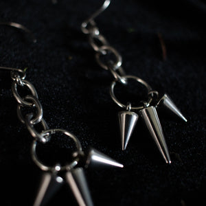 Pair of silver earrings dangling with short and long spikes hanging from chain links.