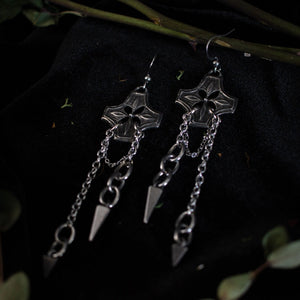 Pair of silver earrings with chained spikes dangling from floral checkered pendant.